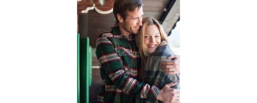 Couple souriant au chalet, femme enveloppée dans un plaid en laine grise – Plaid Addict
