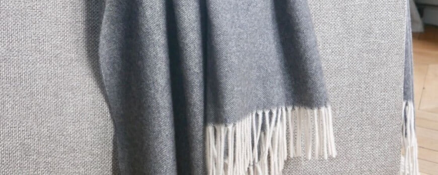 Plaid en cachemire gris à franges blanches drapé sur un canapé – Plaid Addict