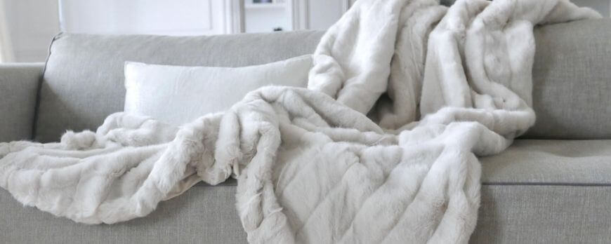 Plaid en fausse fourrure ivoire disposé sur un canapé gris clair – Plaid Addict