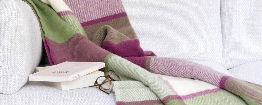 Plaid à carreaux vert, prune et écru sur un canapé avec livre et lunettes – Plaid Addict