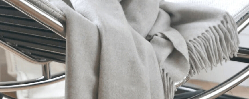 Plaid en cachemire gris clair à franges drapé sur un fauteuil design – Plaid Addict