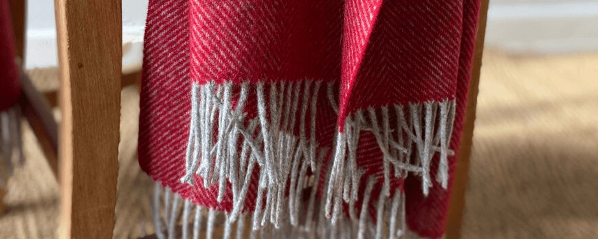 Plaid rouge à chevrons et franges grises suspendu à une chaise en bois – Plaid Addict