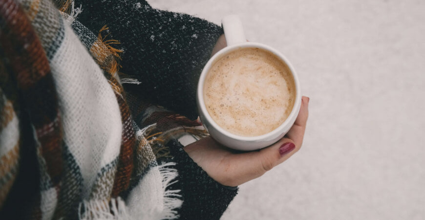 Mains tenant un café chaud, emmitouflées dans un plaid à carreaux sous la neige