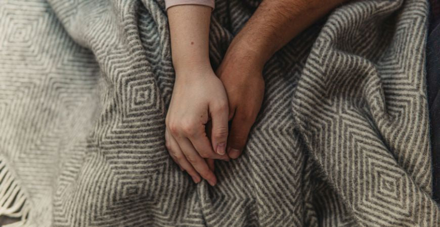 Mains d'un couple enlacées sur un plaid en laine à motifs géométriques gris – Plaid Addict