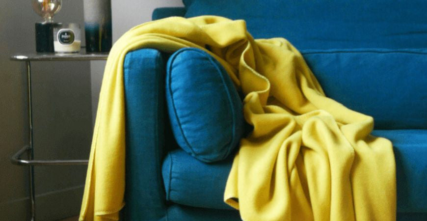 Plaid polaire jaune anis drapé sur un canapé bleu pétrole – Plaid Addict