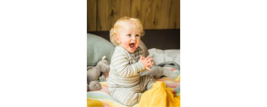 Bébé rieur assis sur une couverture pastel avec ses peluches – Plaid Addict