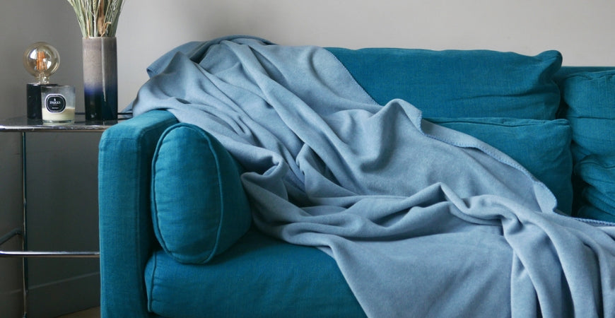 Plaid bleu ciel en maille douce drapé sur un canapé bleu canard – Plaid Addict