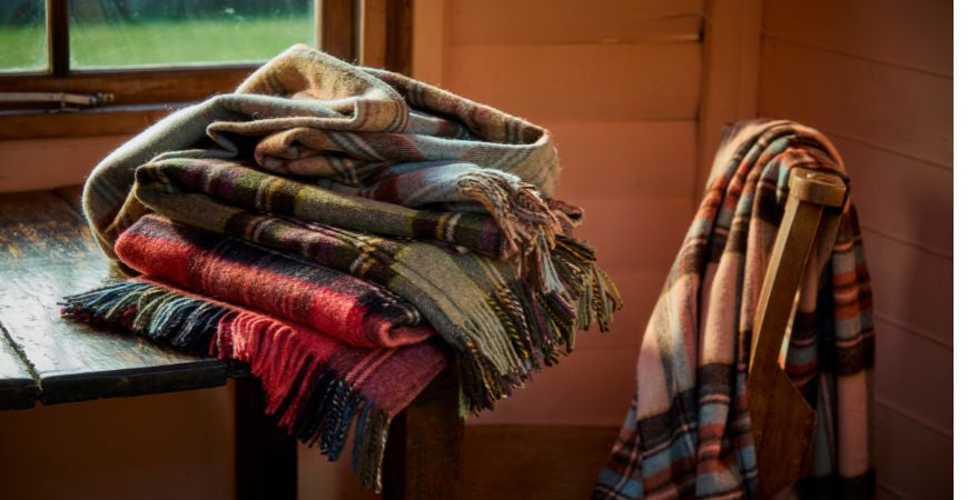 Pile de plaids écossais aux tons automnaux dans une cabane en bois – Plaid Addict
