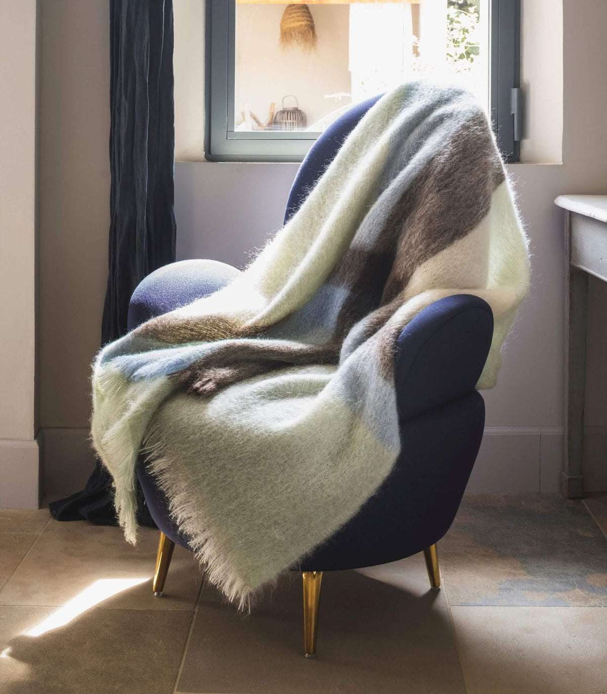 Plaid mohair à carreaux blanc brun et bleu posé sur un fauteuil bleu