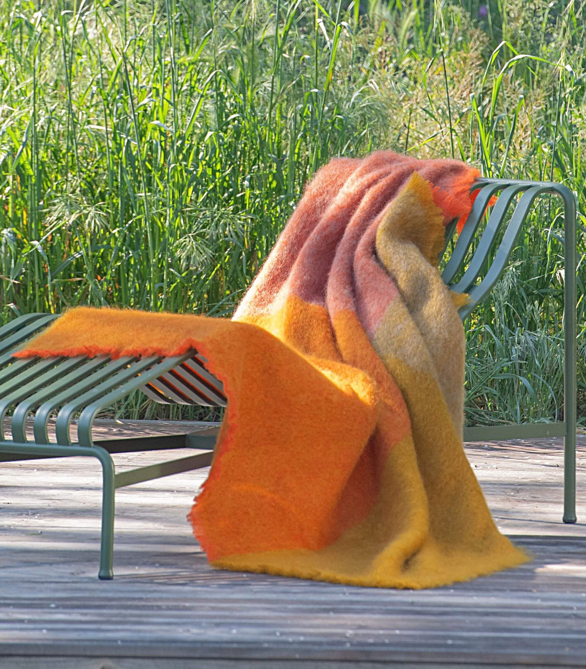 Plaid mohair orange et ocre posé sur un fauteuil extérieur